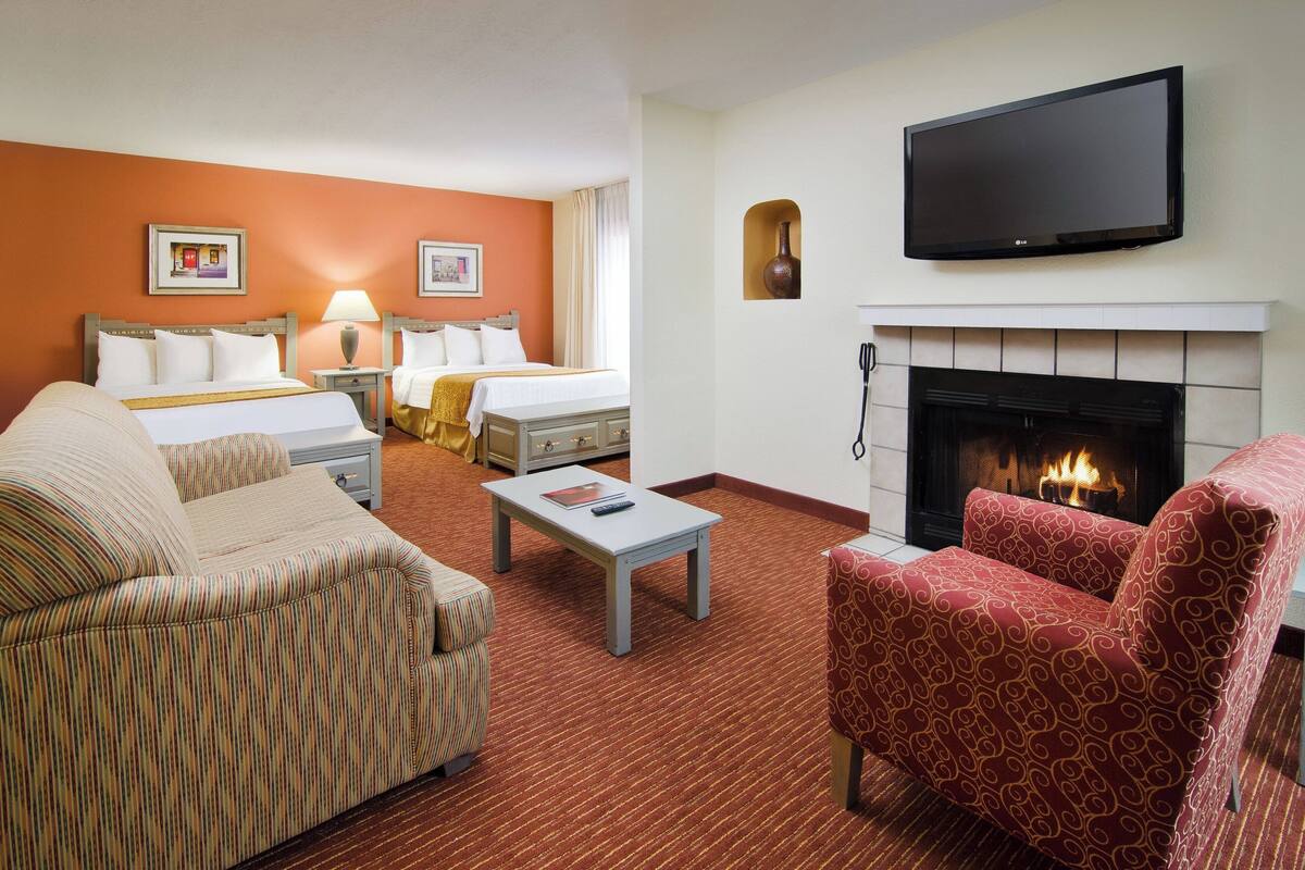 Une chambre d’hôtel avec un lit, un canapé, un fauteuil à motifs, une télévision et une cheminée.