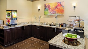 A hotel kitchen with a self-serve beverage station, a large colorful painting on the wall, and a bowl of green apples on the counter. - Residence Inn by Marriott Santa Fe (Santa Fe)