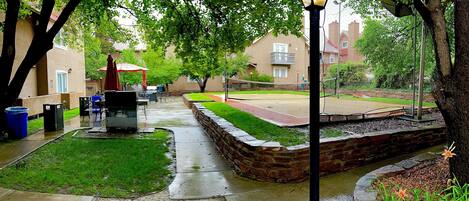 A courtyard with a stone pathway, a small lawn, and a tennis court.