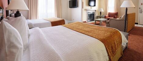 Quarto de hotel com duas camas, televisão, lareira, escrivaninha e uma cadeira.