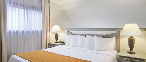 A hotel room with a large bed, two bedside tables with lamps, a ceiling fan, and a window with curtains.