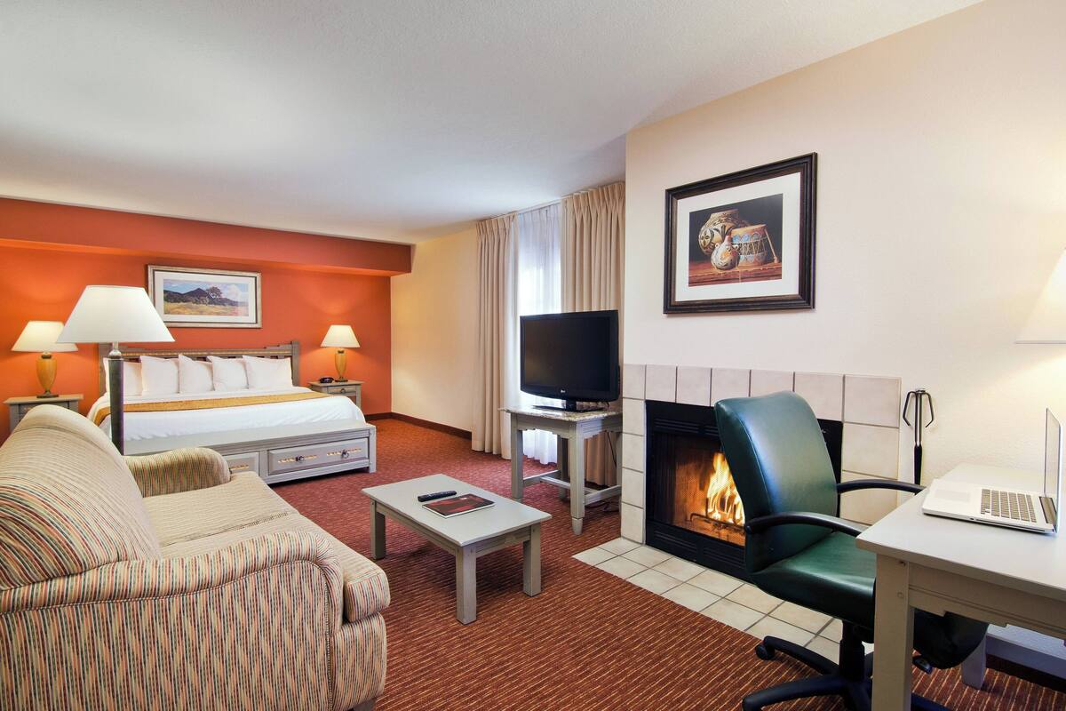 Une chambre d’hôtel comprenant un lit, deux canapés, une télévision, une cheminée et un bureau avec un ordinateur portable.
