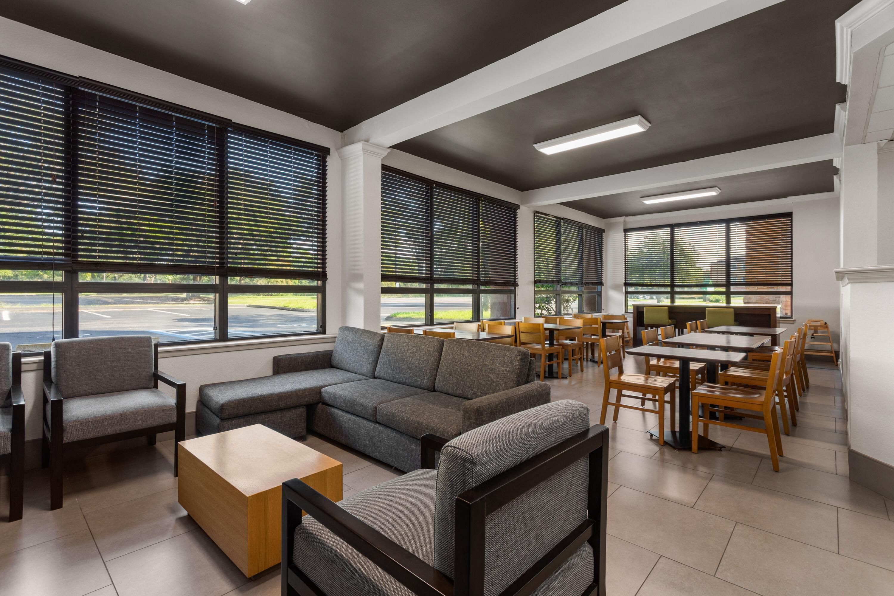 A modern interior with a sectional sofa, chairs, a wooden coffee table, and a dining area with tables and chairs.