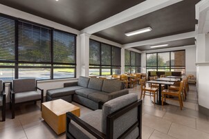 Um interior moderno com sofá modular, cadeiras, mesa de centro de madeira e área de jantar com mesas e cadeiras.