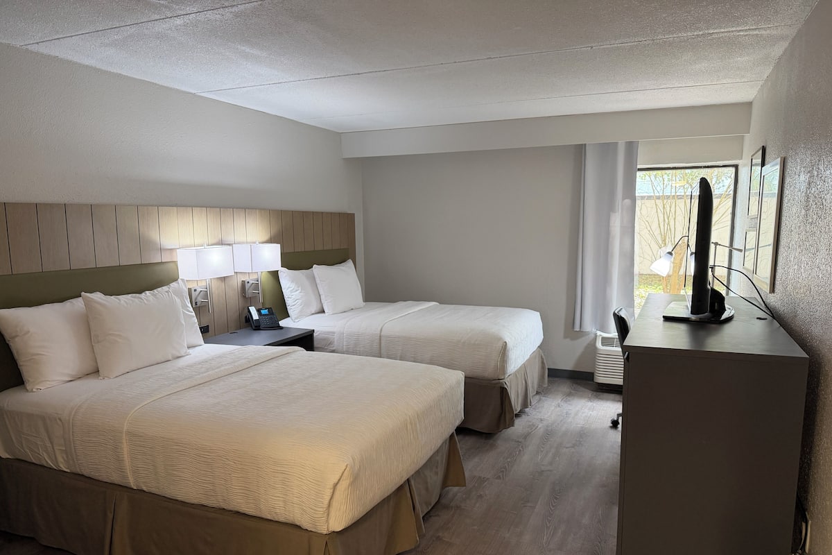 A hotel room with two beds, a desk with a lamp, a television, and a window with curtains.
