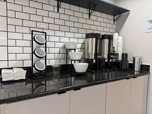 Una cocina con encimera negra, salpicadero de azulejos blancos y diversos electrodomésticos.