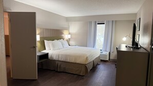 Una habitación de hotel con cama, lámparas de noche, un escritorio con lámpara y una ventana con cortinas.