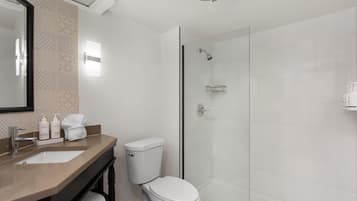 A modern bathroom with a glass-enclosed shower, a white toilet, a vanity with a mirror, and toiletries.