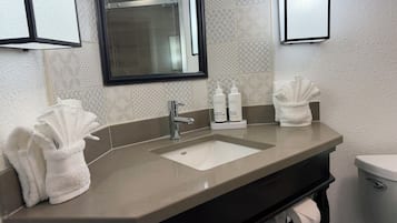 A bathroom with a sink, two bottles of hand soap, and two towels.