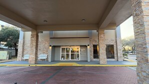 Una entrada techada con fachada de ladrillo, un banco y un camino despejado que conduce a la entrada del edificio.
