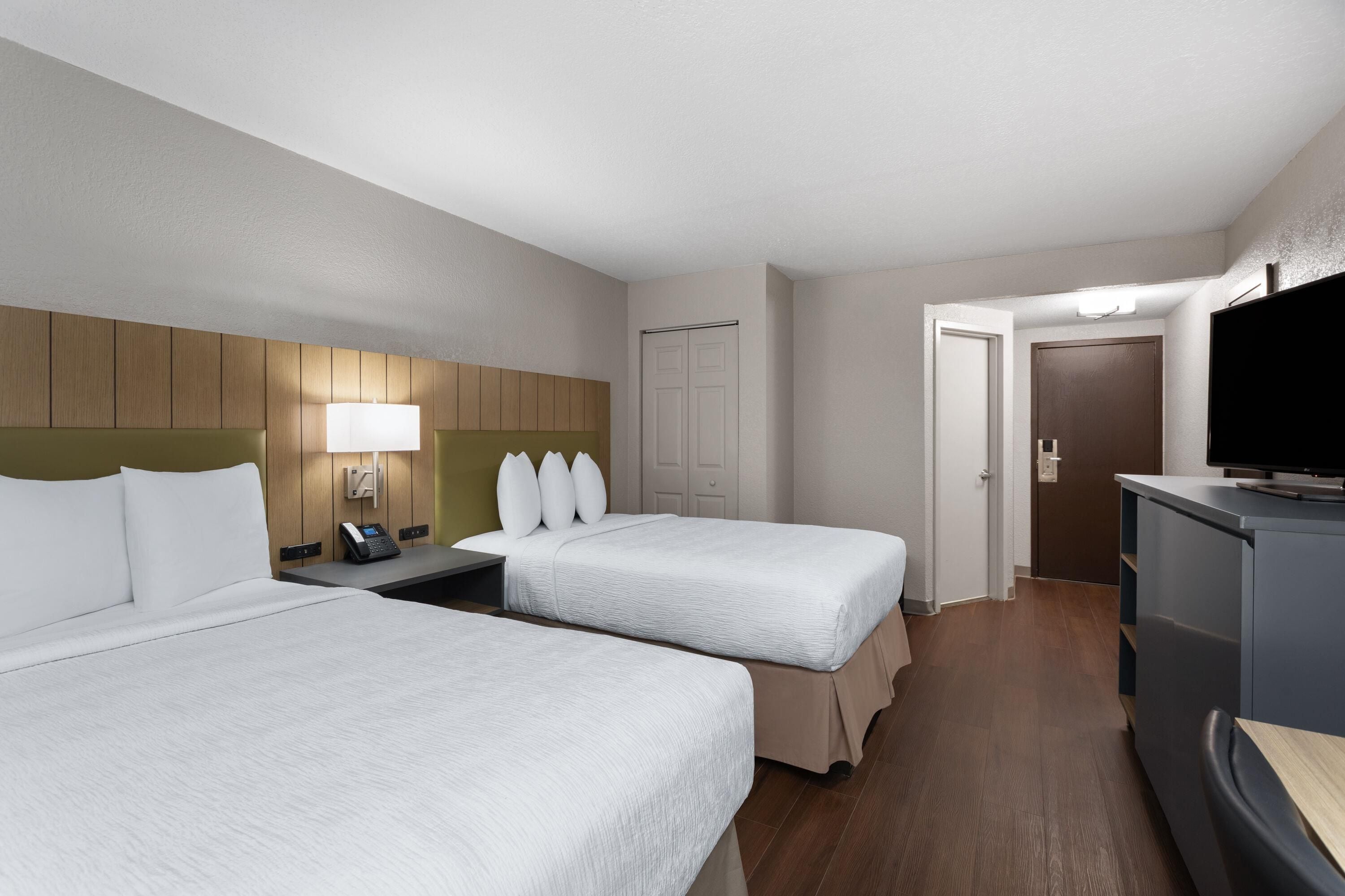 A hotel room with two beds, a desk with a telephone, a television, and a door leading to another room.