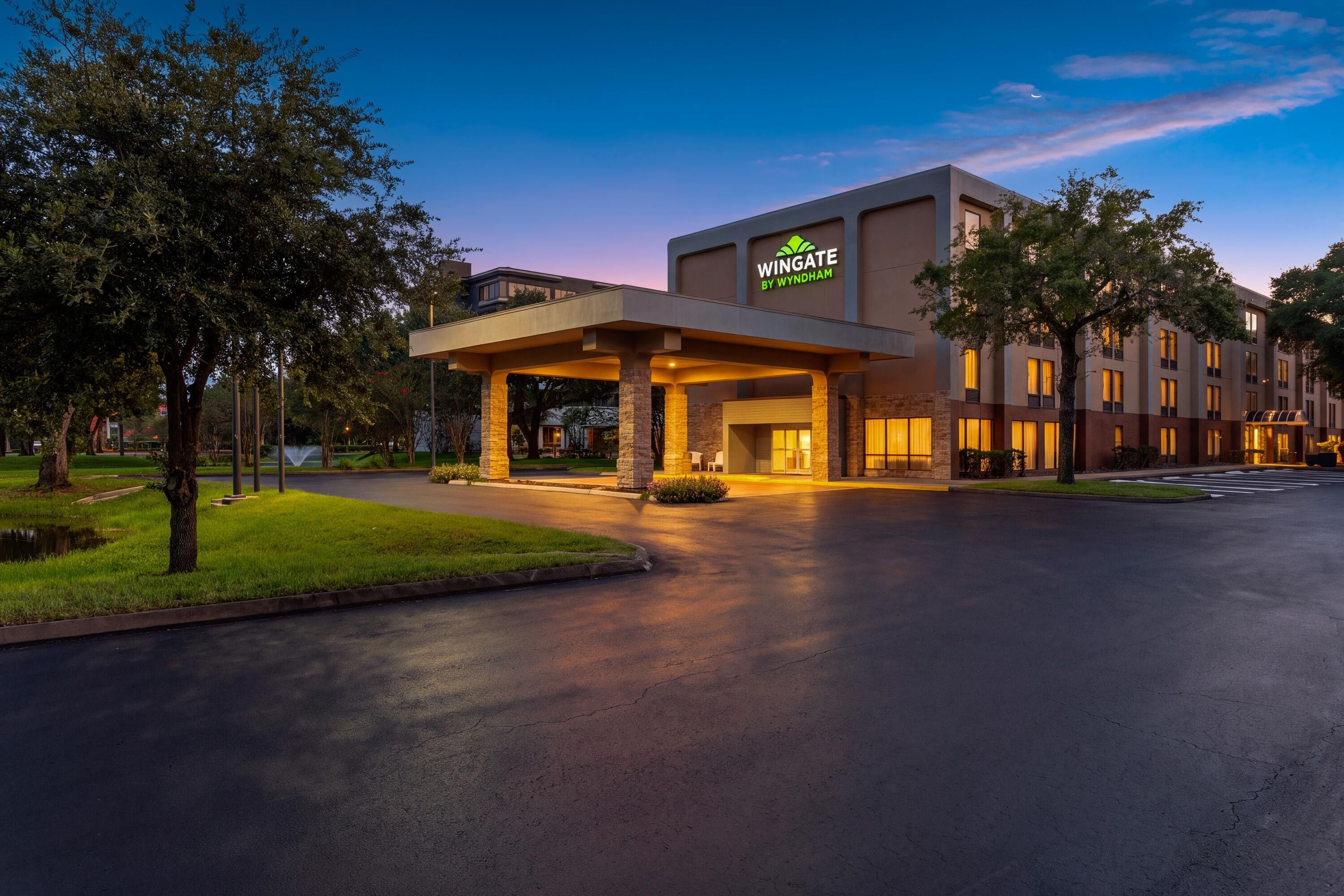 A Wingate by Wyndham hotel with a modern design, featuring a covered entrance and a well-maintained lawn.