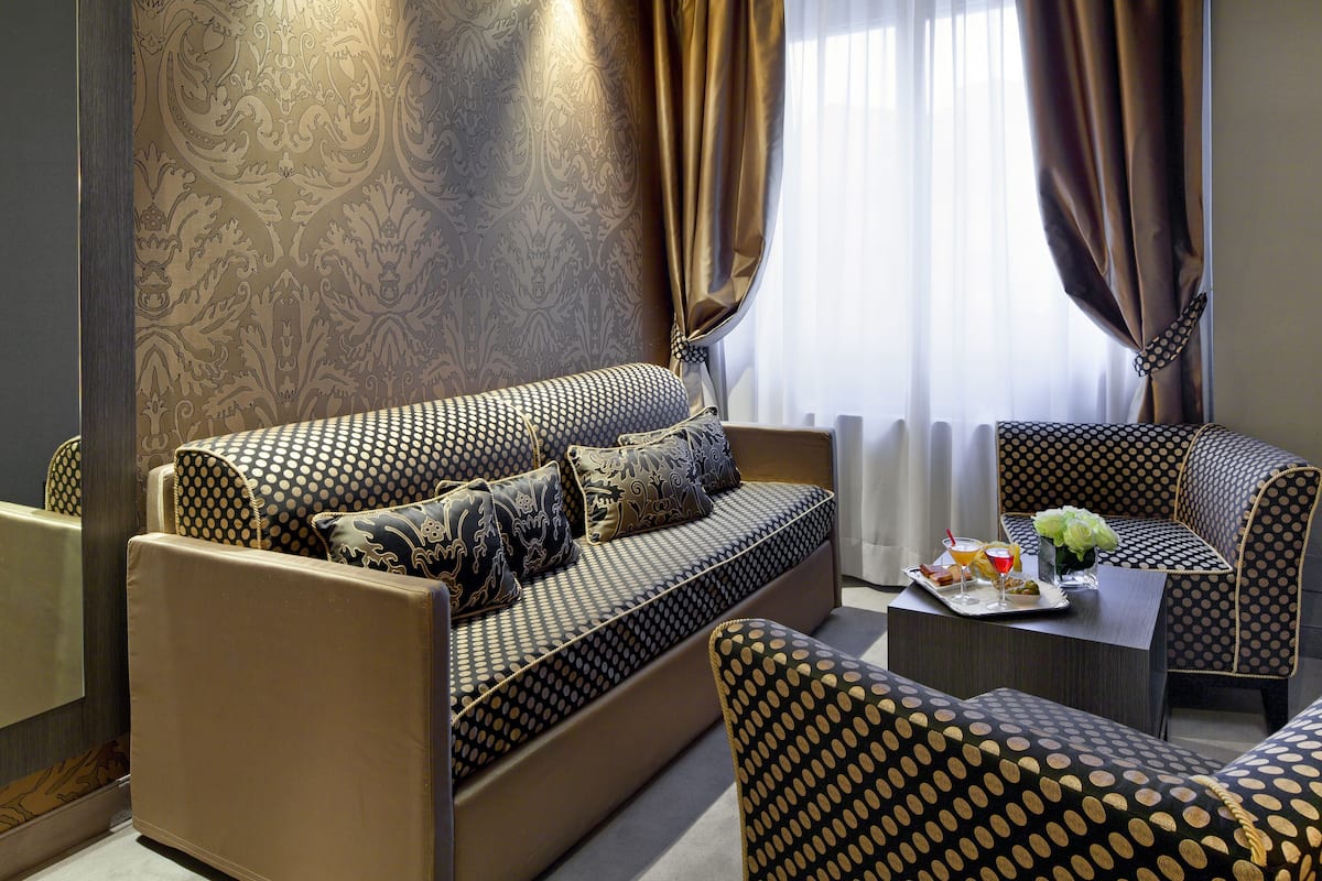 Een moderne woonkamer met een gestreept bankje, bijpassende fauteuils en een eettafel gedekt met een dienblad eten en drinken.