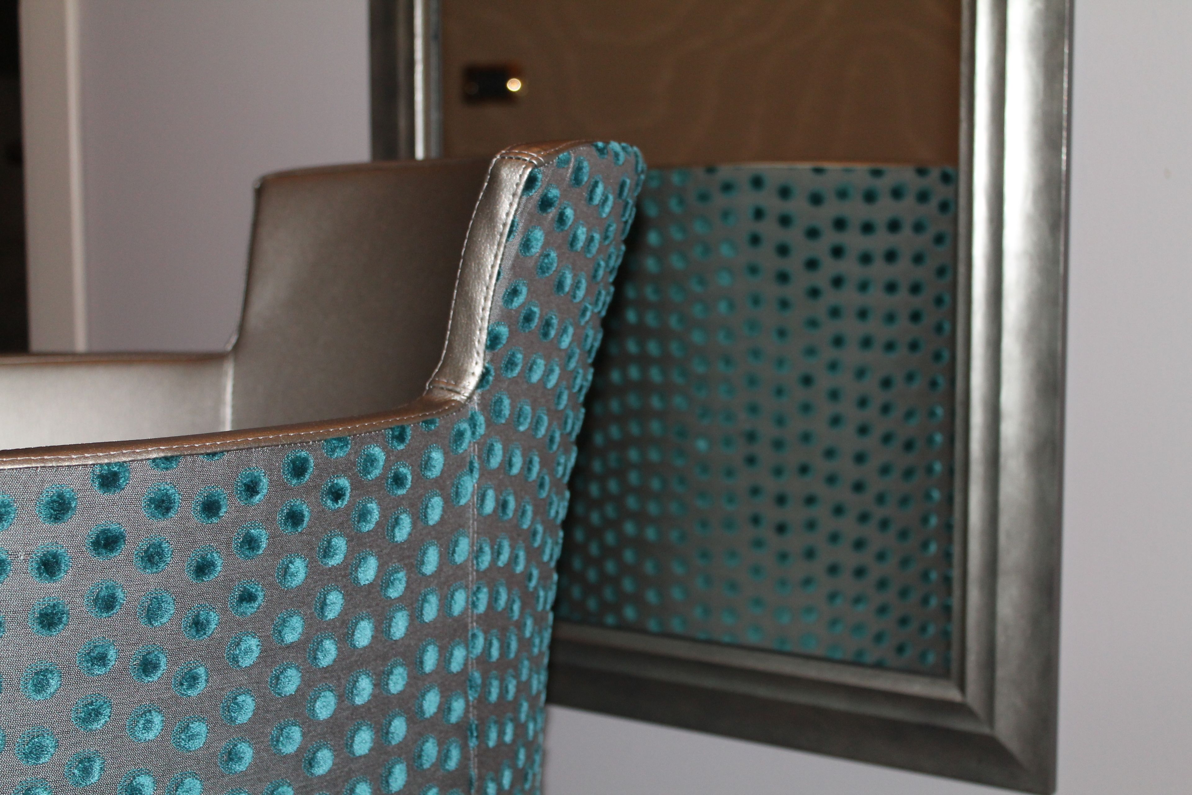 A close-up of a teal-patterned armchair with a metallic frame, reflecting in a mirror.