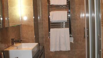 Un baño moderno con un lavamanos grande, un espejo, un perchero con tres toallas, un taburete pequeño y una zona de ducha.