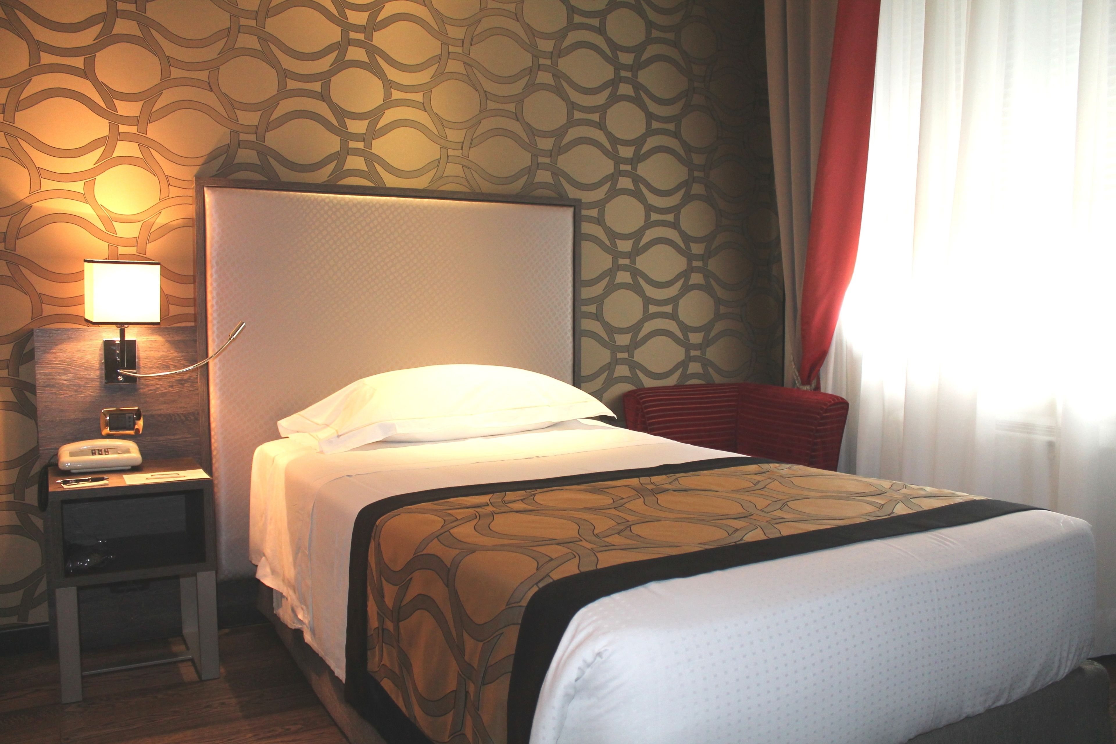 Ein Hotelzimmer mit einem Bett, einem Nachttisch mit Lampe und einer Wand mit Muster.