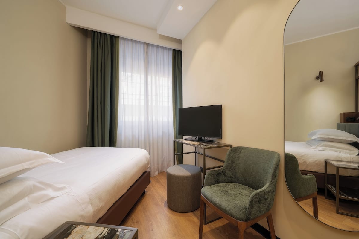 Een hotelkamer met een bed, een stoel, een televisie en een spiegel.
