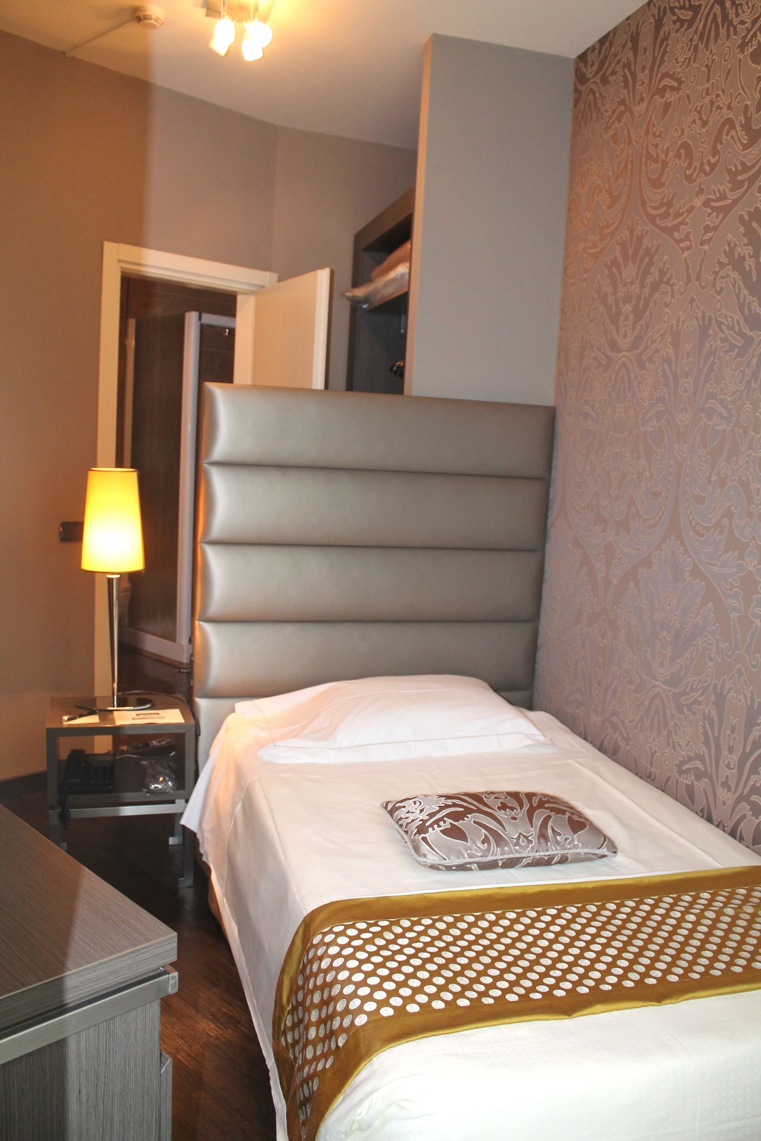 Een hotelkamer met een bed, nachtkastje, lamp en een behang met patroon.