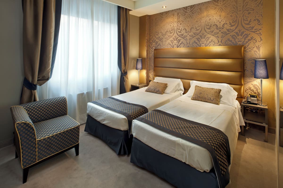 Een hotelkamer met twee bedden, een slaapbank en een nachtkastje met een lamp.