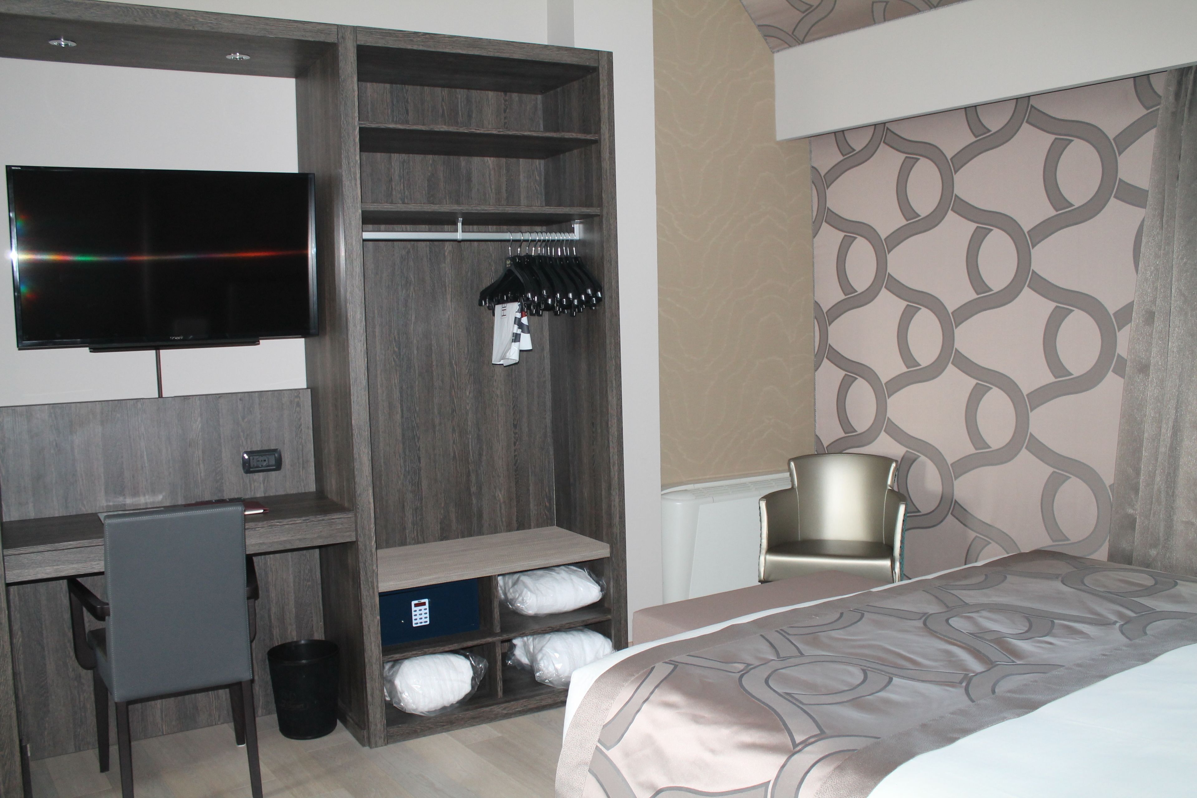 Una habitación de hotel con cama, escritorio, silla, armario y televisor.
