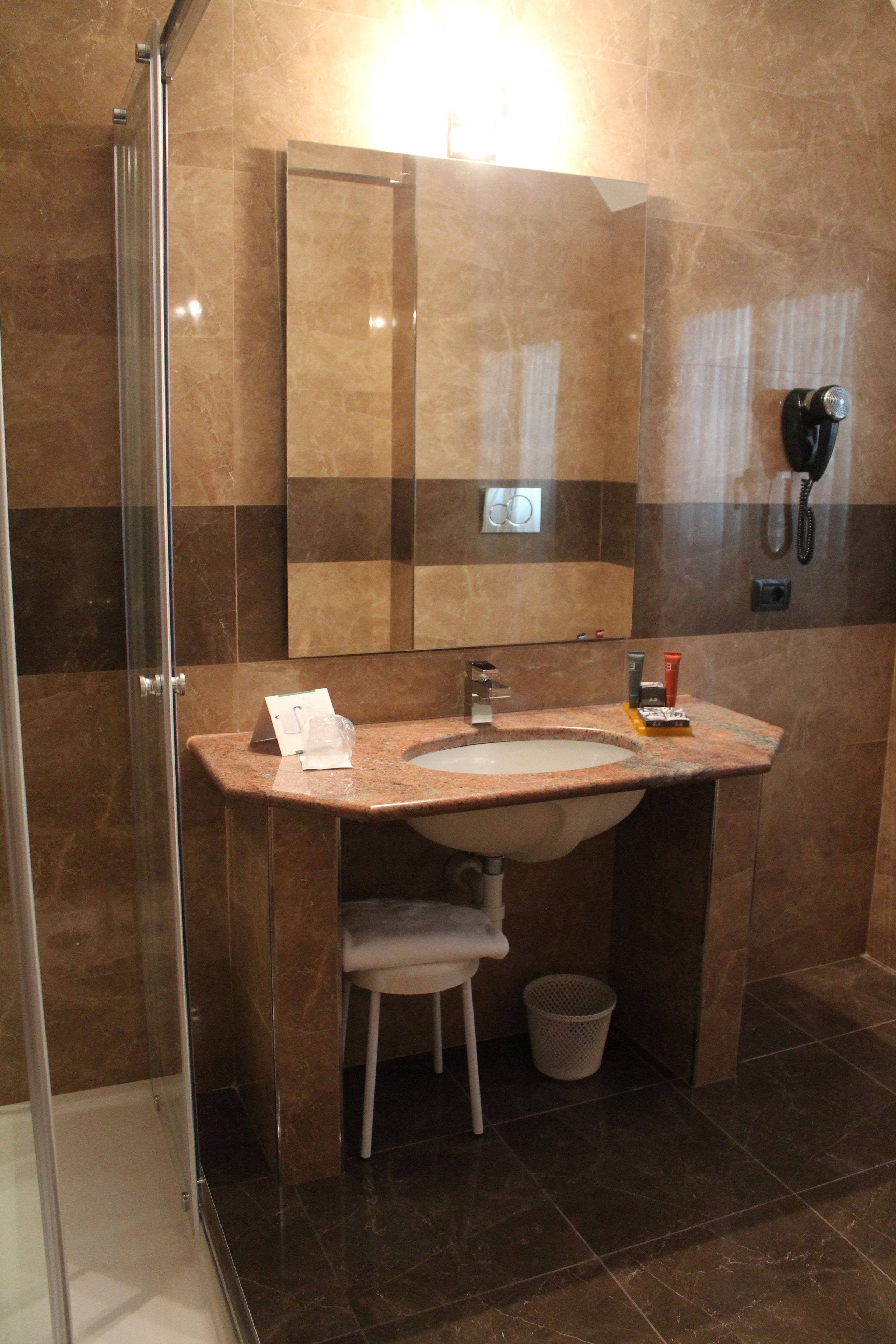 Une salle de bain avec un lavabo en marbre, une cabine de douche en verre, un miroir et un téléphone.