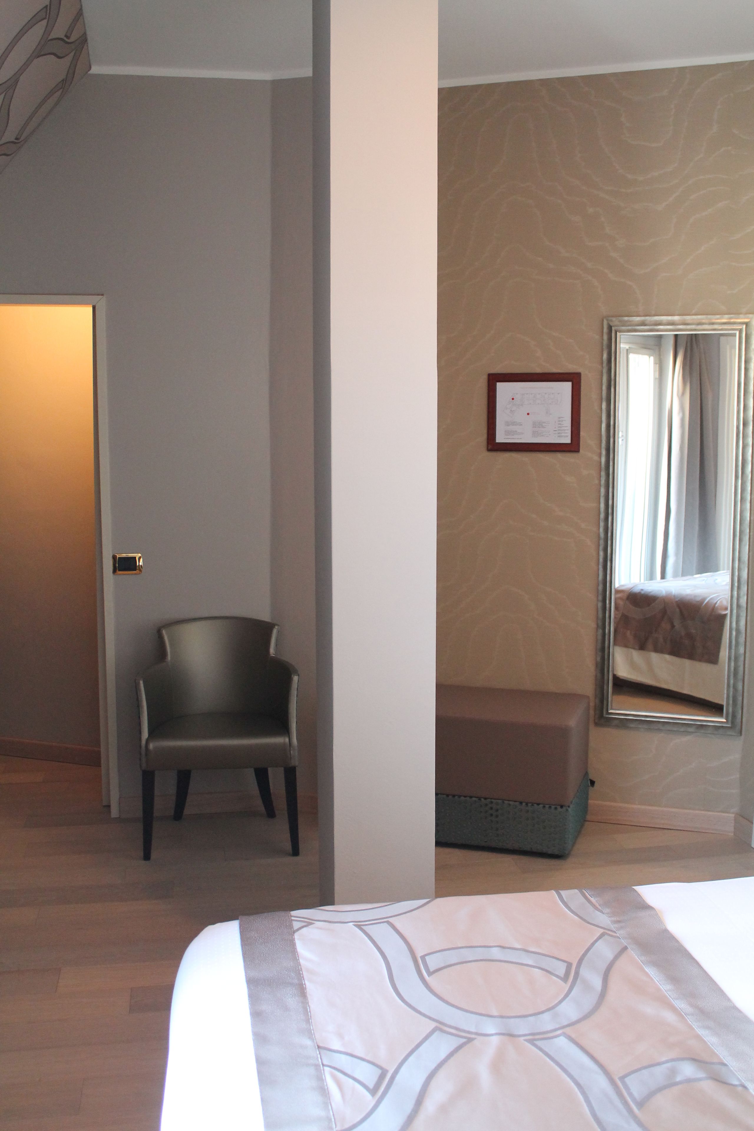 A hotel room with a bed, a chair, a bench, a mirror, and a door.