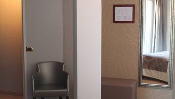 A hotel room with a bed, a chair, a bench, a mirror, and a door.