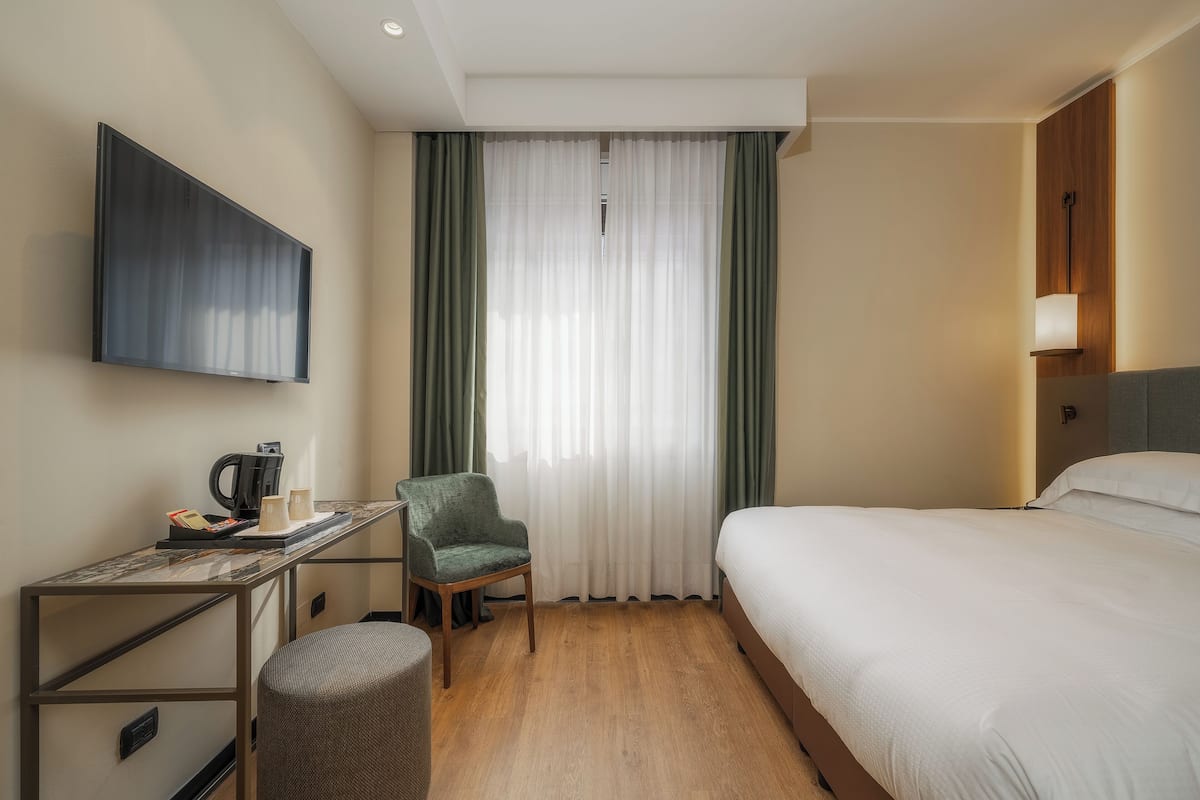 Hotelkamer met een bed, een bureau met koffiezetapparaat, een stoel en een televisie aan de muur.