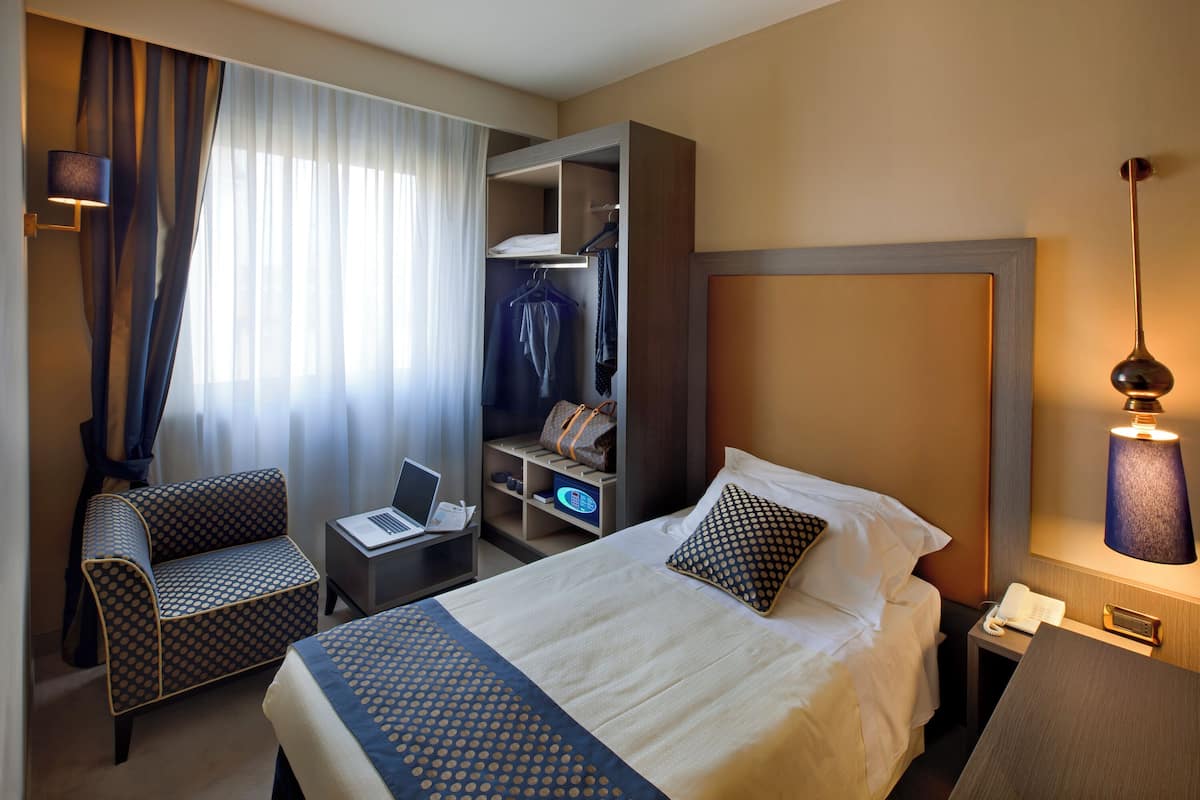 Hotelkamer met een bed, bureau met een laptop, stoel, garderobe en nachtkastje met lamp.