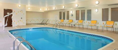 An indoor swimming pool with a blue tiled edge, surrounded by yellow chairs and a clock on the wall.