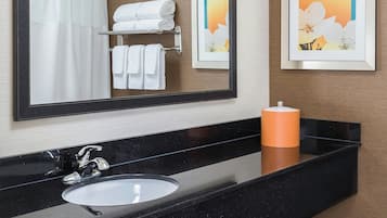 A bathroom with a black countertop, white sink, and a large mirror. There are towels on a shelf and a framed picture on the wall.