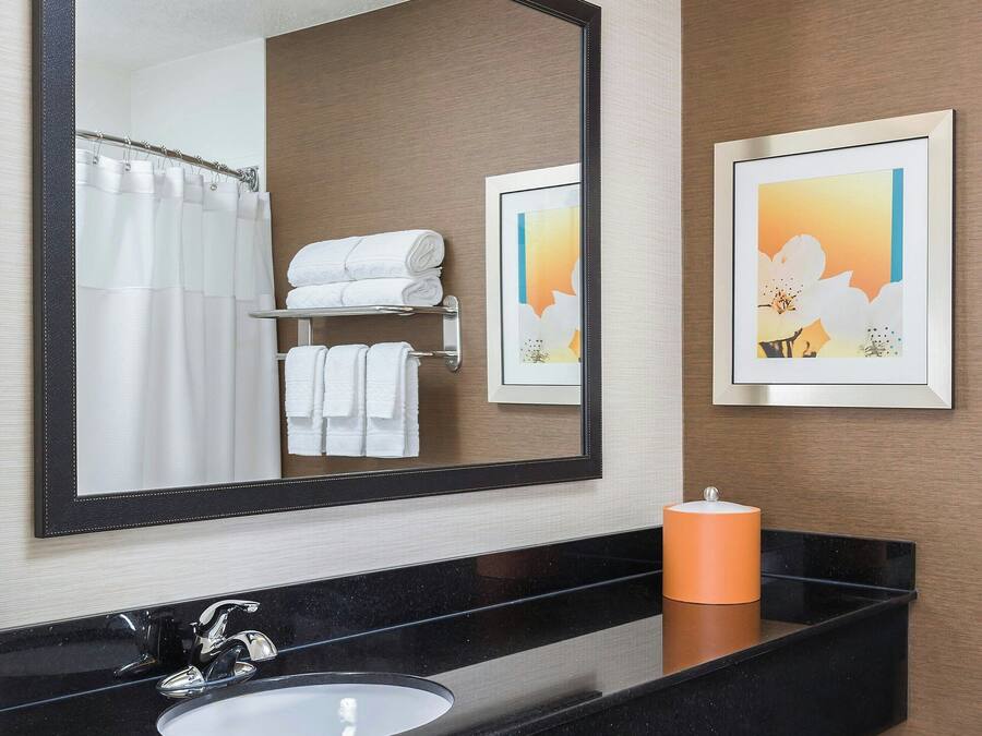 A bathroom with a black countertop, white sink, and a large mirror. There are towels on a shelf and a framed picture on the wall.