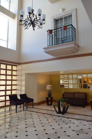 A spacious lobby with a high ceiling, a chandelier, a balcony with potted plants, a sofa, and a coffee table. - iStay Hotel Ciudad Juarez (Ciudad Juárez)