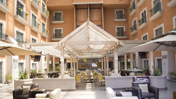 A spacious indoor courtyard with multiple seating areas, a central dining space, and a covered area with a triangular roof. - iStay Hotel Ciudad Juarez (Ciudad Juárez)