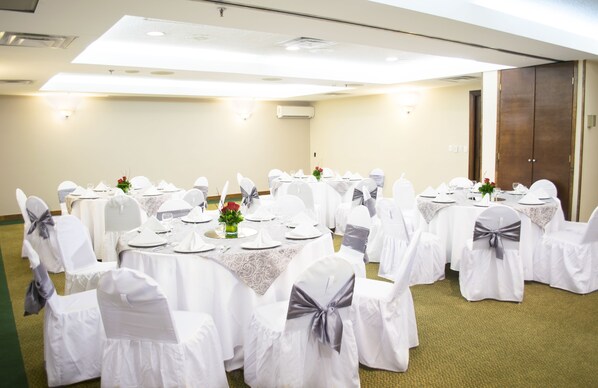 Un salón de conferencias con mesas redondas, manteles blancos y sillas con cintas grises.