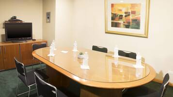 Une salle de conférence avec une grande table ovale, six chaises, un téléviseur posé sur un meuble et des bouteilles d’eau sur la table.