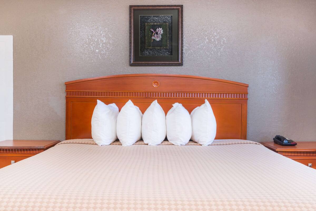 A neatly made bed with a patterned bedspread and five pillows. A framed picture hangs on the wall above the bed.