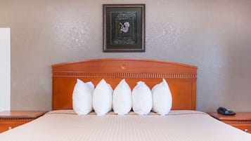 A neatly made bed with a patterned bedspread and five pillows. A framed picture hangs on the wall above the bed.