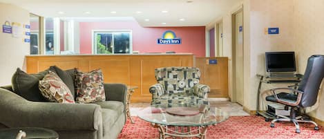 Un hall de hotel con mostrador de recepción, un sofá, un sillón estampado, una mesa de centro de vidrio y un televisor.