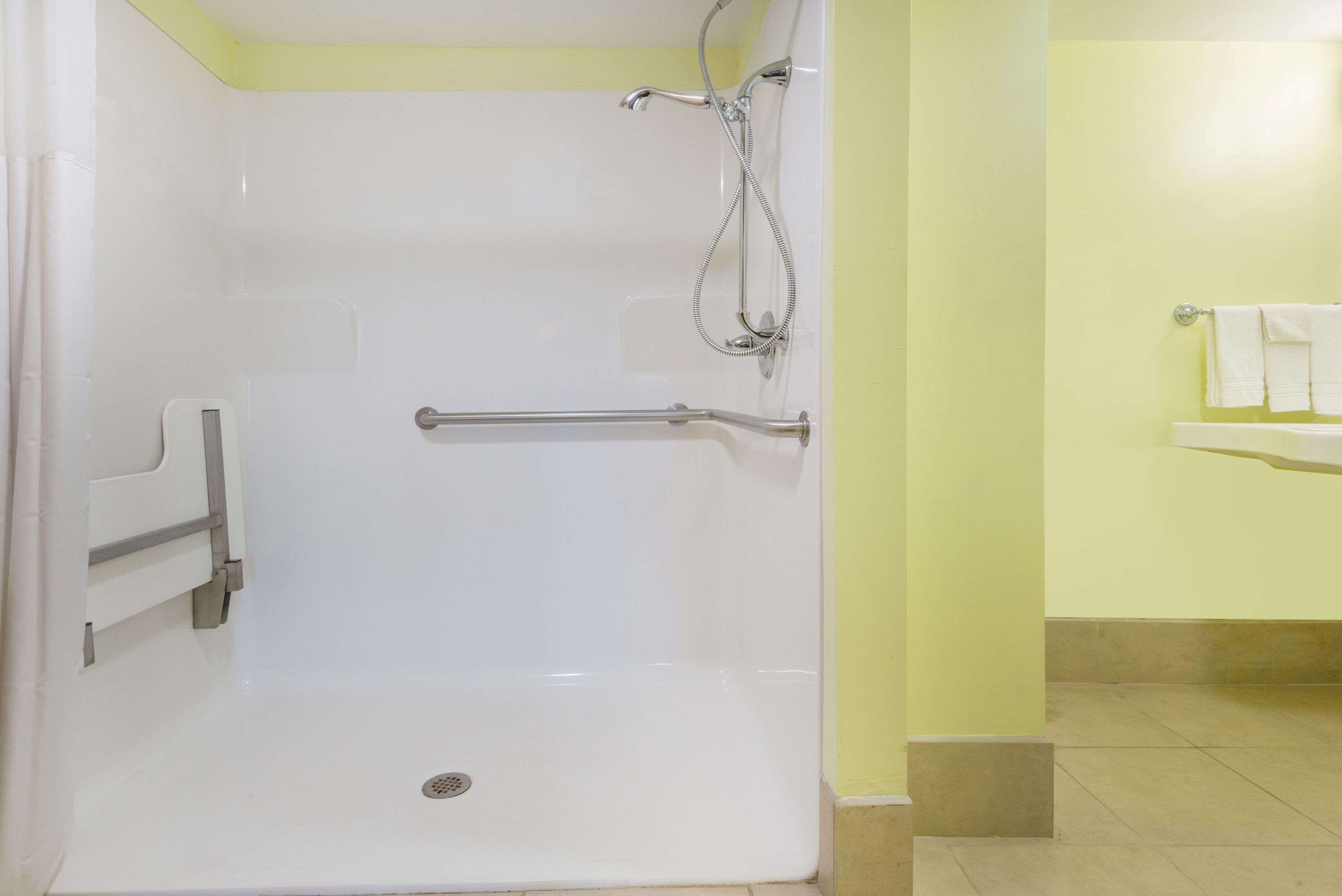 Ducha a nivel con barandilla, cabezal de ducha de mano y soporte para papel higiénico.
