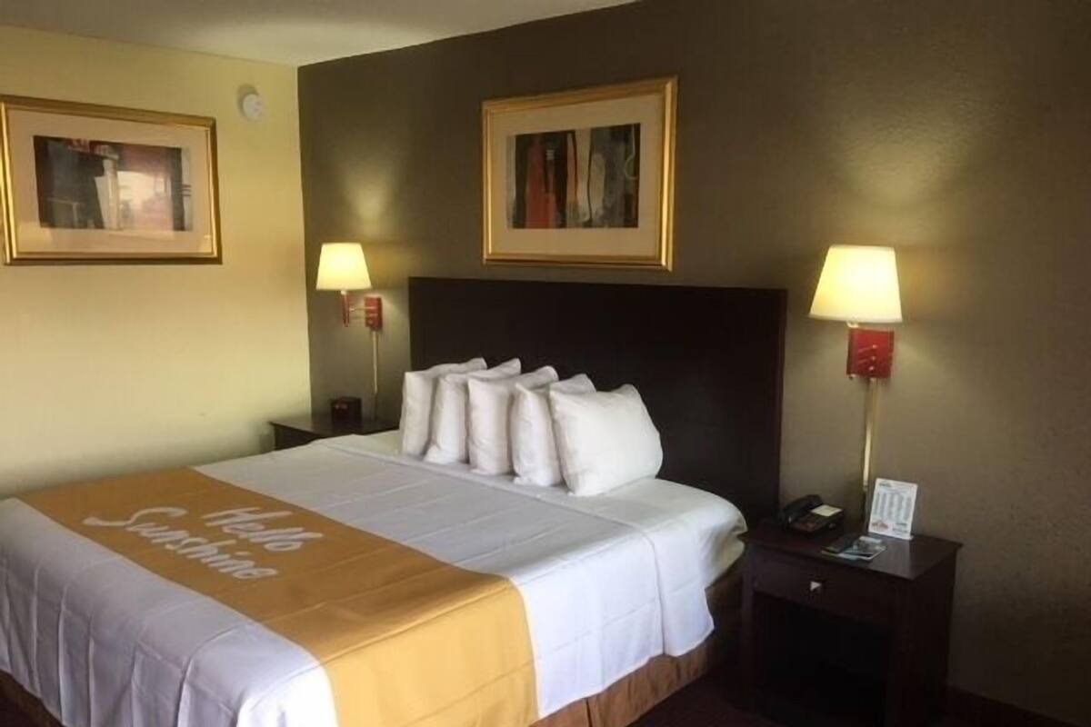 A hotel room with a large bed, two bedside tables, a nightstand, and two wall-mounted lamps.