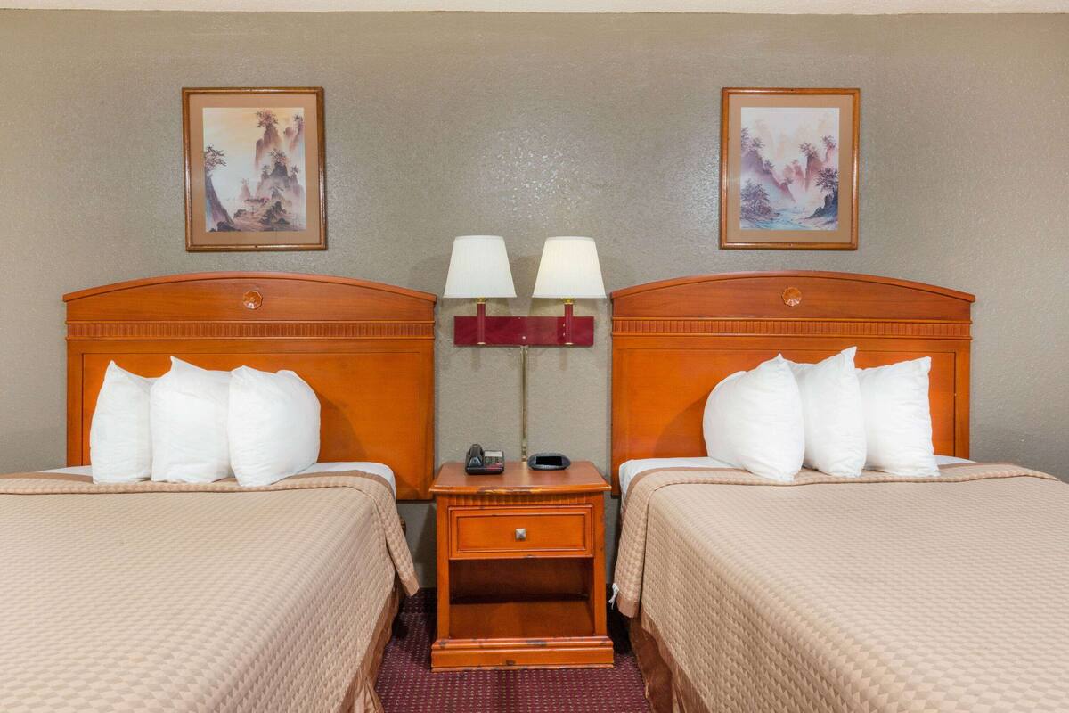 A hotel room with two beds, a nightstand with lamps, and two framed pictures on the wall.