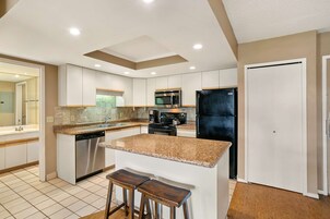 A modern kitchen with white cabinets, granite countertops, stainless steel appliances, and a central island with stools.