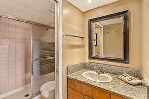 A bathroom with a glass shower enclosure, a sink with a marble countertop, and a wooden vanity.