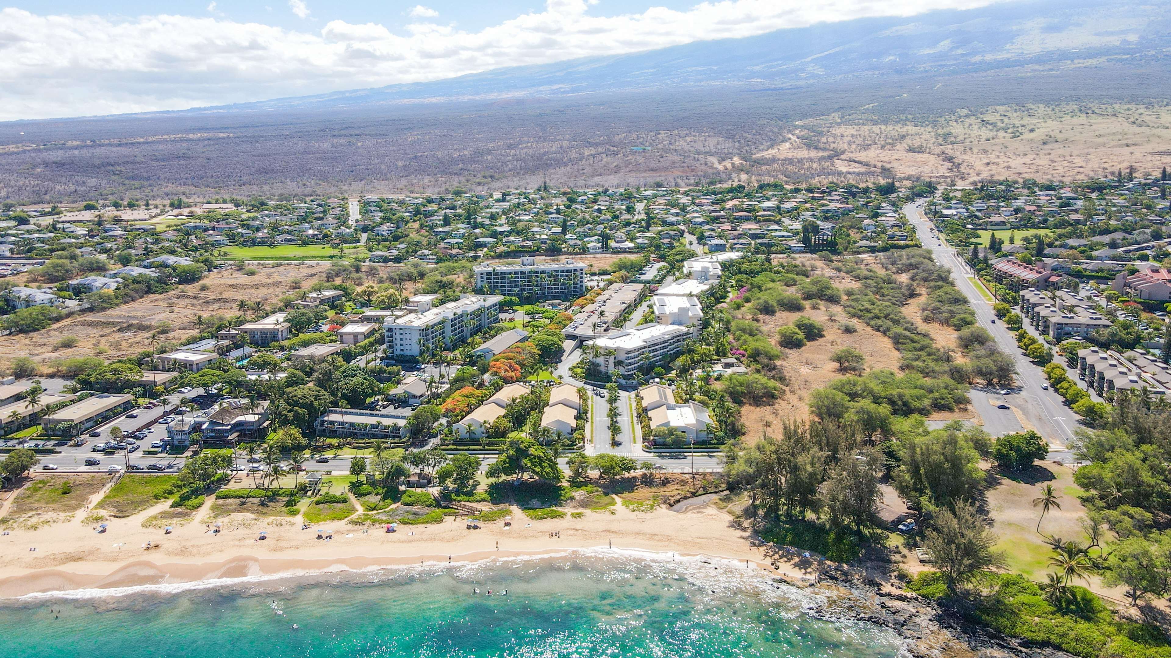 An aerial view of a coastal residential area with beachfront properties, roads, and buildings.
