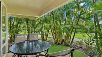 An outdoor patio with a round table and chairs, surrounded by lush greenery and palm trees.
