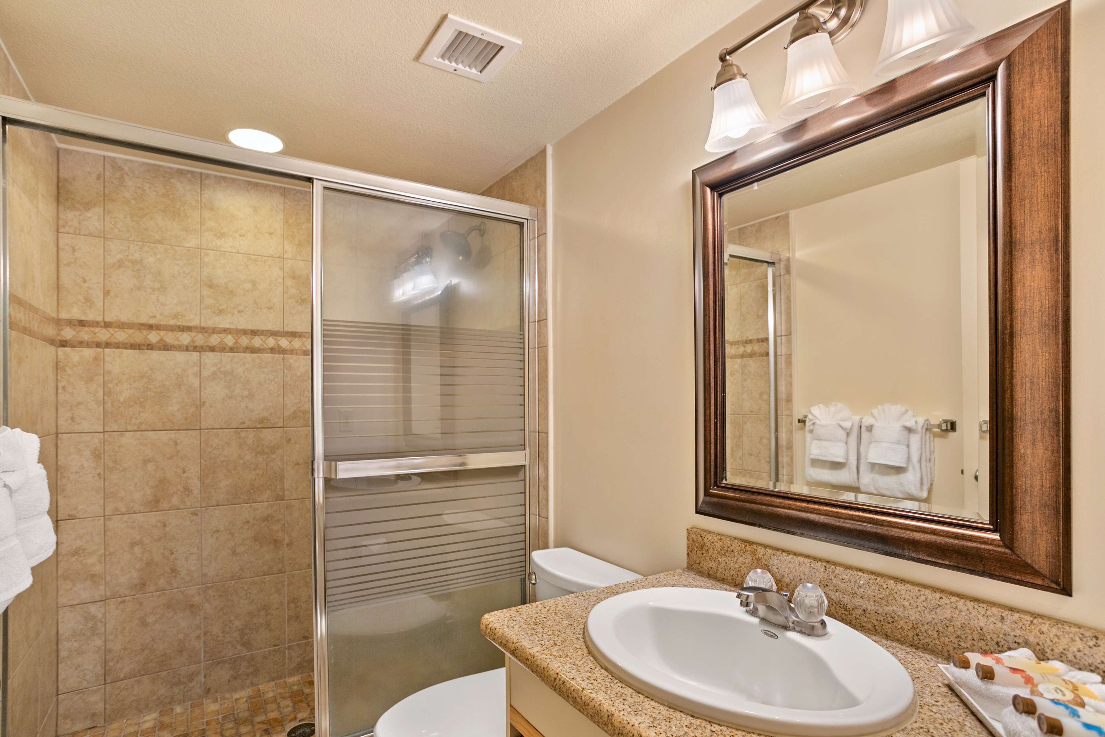 A bathroom with a glass-enclosed shower, a sink with a vanity, and a large mirror.