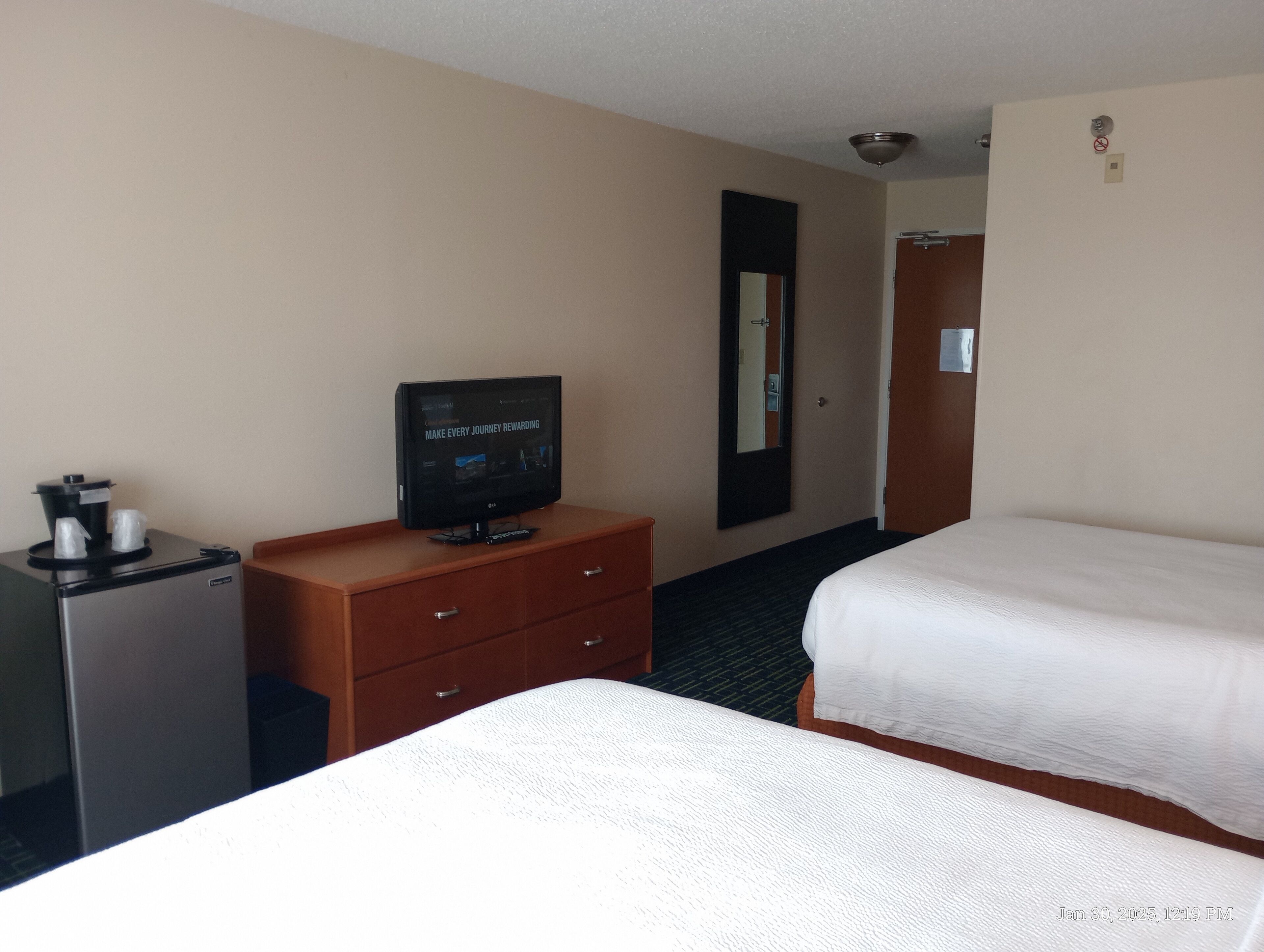 Habitación de hotel con dos camas, un televisor sobre un aparador de madera, una cafetera y un espejo en la pared.