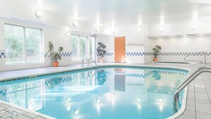 An indoor swimming pool with clear water, tiled walls, and potted plants.