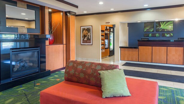 A hotel lobby with a red sofa, a fireplace, a reception desk, and a wall-mounted TV.